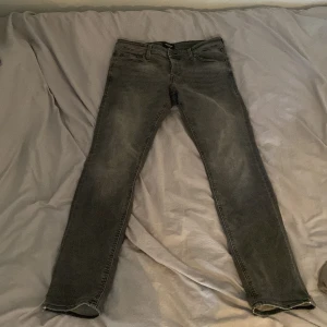 Grå jeans från Jack & Jones - Grå Slim Glenn jeans från Jack & Jones med en klassisk femficksdesign. De har knappar framtill. Perfekta för en stilren look. Storlek 31/34