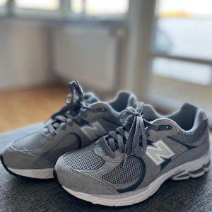 Grå sneakers från New Balance - Snygga grå sneakers från New Balance med klassisk design. Skorna har en ovandel i mesh och mocka med snörning för en bekväm passform. Perfekta för en stilren vardagslook. Helt oanvända