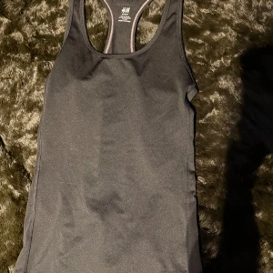 Svart linnetopp från H&M Sport - Säljer en svart linnetopp från H&M Sport. Perfekt för träning med sin bekväma passform och stilrena design. Toppen har en brottarrygg och är tillverkad i ett mjukt och stretchigt material.