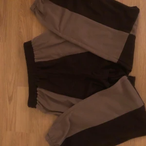 Svart och grå mjukisbyxor - Bekväma mjukisbyxor i svart och grått med elastisk midja. Perfekta för en avslappnad dag hemma eller lättare träning. Byxorna har en enkel design med kontrasterande färgblock.