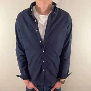 Mörkblå Ralph Lauren skjorta - Nu säljer vi ännu en fet polo skjorta som passar till alla tillställningar! OBS Skjortan saknar en knapp i ena ärmslutet och är ganska urtvättad vilket gör att vi sänker priset rejält! Du ska kunna uttrycka stil utan att det kostar för mycket!🕺🍾💼🤩  Storlek👔: M Nypris💰: ca 1499 kr