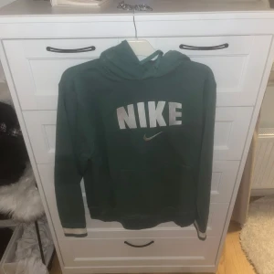 Grön hoodie från Nike - Säljer en grön hoodie från Nike med stor logga på bröstet. Tröjan har långa ärmar och en klassisk huva. Perfekt för en avslappnad stil. Hör av dig vid intresse!