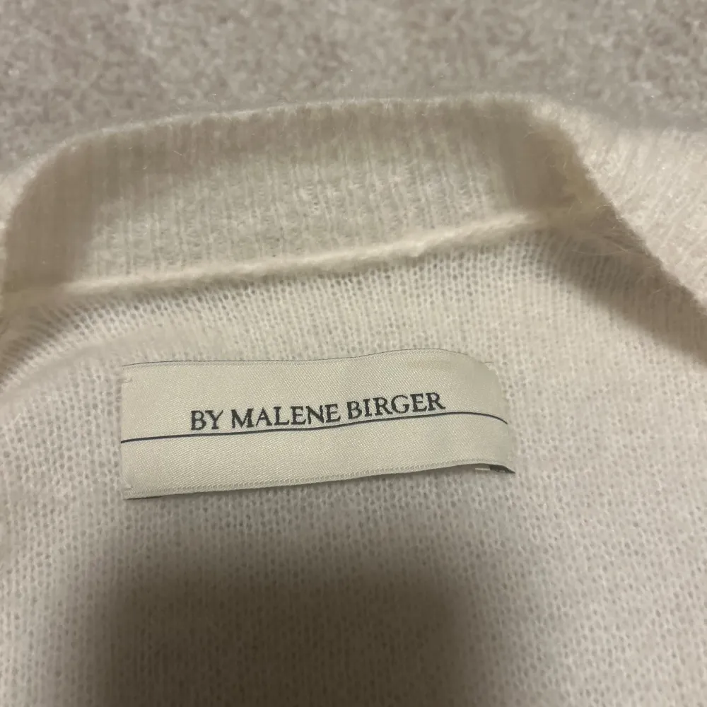 Säljer en elegant vit kofta från By Malene Birger. Den är lång och har långa ärmar med ribbade muddar. Perfekt för att hålla sig varm och stilren under kyligare dagar. Koftan har en öppen design utan knappar, fickor fram och korta sprunn i sidan.. Neuletakit & Villapaidat.