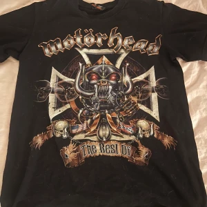 Svart Motörhead t-shirt - Cool svart t-shirt med Motörhead-tryck fram och bak. Framsidan har ett stort, detaljerat motiv med bandets ikoniska logga och grafik. Perfekt för rockälskare och fans av bandet.