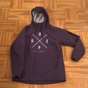 Jacka från Dope - Säljer en snygg lila anorak från Dope med vit logga framtill. Jackan är i riktigt bra skick🤩Jackan har en huva med snörning och en praktisk ficka på ärmen. Perfekt för vintersport och håller dig varm i backen. Den har ficka för liftkort på armen och en ficka med mobilhållare i på magen