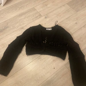 Svart stickad bolerotopp från Zara - Säljer en svart stickad bolerotopp från Zara. Toppen är croppad med långa ärmar och har ett fint mönster. Perfekt för att lägga till en extra touch till din outfit.