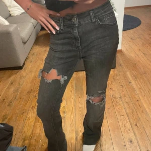 Grå jeans med slitningar - Snygga svarta jeans med slitningar på knäna. De har en bootcut-stil och är midwaist. Midjemått: ca 34cm rakt över och innerbenslängd: ca 84cm🥰