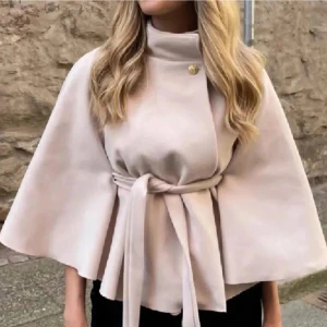 Beige kappa med knytband - Elegant beige kappa med knytband i midjan och en knappdetalj vid halsen. Den har vida ärmar och en stilren design som passar perfekt för höst och vår. Perfekt för att ge en sofistikerad touch till din outfit. Nypris var 800kr.