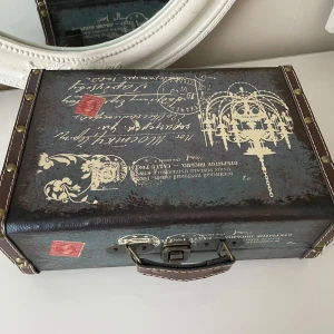 Vintage-inspirerad case trä låda med tryck - Säljer en unik vintage-inspirerad  intage Case Trä Minneslåda  ett coolt tryck av en ljuskrona och gammaldags text. har en mörk färg med skinn band och nitar längs kanterna. Perfekt för att ge en retro touch till din stil!.måttet är 30x20 cm .jag kan möta er i Stockholm utanför Åhléns 