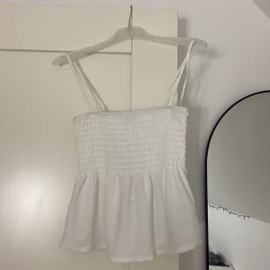 Offwhite smockad linnetopp - Säljer en söt offwhite smockad linnetopp med smala axelband. Toppen har en smockad överdel och en lätt utsvängd nederdel som ger en fin passform. Toppen är aldrig använd & banden går o ta av 💞