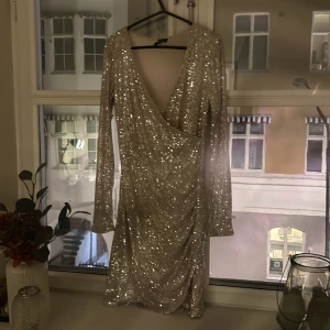 Glittrig silverklänning - Snygg glittrig klänning i silver med omlott-design och v-ringning. Klänningen har långa ärmar och en tight passform som framhäver figuren. Perfekt för en festlig kväll! Endas använd under ett nyår ✨