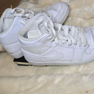 AIR JORDAN 1 MID - Snygga vita Nike-Jordan sneakers med hög design och klassisk snörning. Perfekta för en stilren look. Skorna har en vit sula och är tillverkade i både läder & syntetmaterial. 