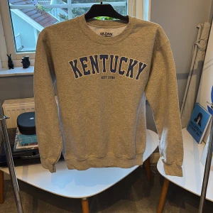 Grå sweatshirt med blått tryck. - En grå sweatshirt med texten 'Kentucky EST 1792' i blått på framsidan.