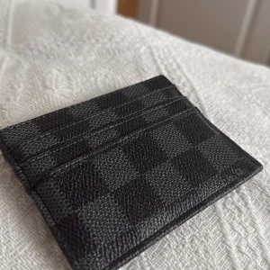 Svart rutig korthållare - Snygg och kompakt svart plånbok/korthållare med ett stilrent klassiskt rutigt mönster. Perfekt för att hålla dina kort organiserade. Den är liten och smidig att ha med sig överallt.