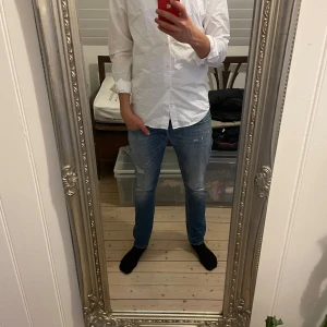 Vit skjorta med långa ärmar - Säljer en stilren vit skjorta med långa ärmar. Perfekt för en klassisk look. Skjortan har knappar framtill och är tillverkad i ett lätt och bekvämt material. Vet inte vad märket heter men det ses på bild två. Säljer billigt för har inte kommit till användning! Priset kan såklart diskuteras!