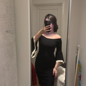 Svart offshoulder klänning från Vesper - Elegant svart offshoulder midiklänning från Vesper med vita detaljer på ärmarna. Klänningen har en tight passform och trekvartsärmar, perfekt för en stilren look. Helt oanvänd med prislapp kvar. Unik, utgången modell!🌟