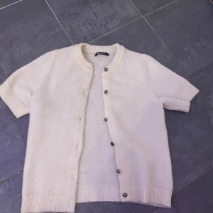 Vit kofta från Gina Tricot - Säljer en söt vit kofta från Gina Tricot i storlek XS. Koftan har korta ärmar och knappar framtill. Perfekt för lager-på-lager och att hålla sig varm med stil. 🧥✨