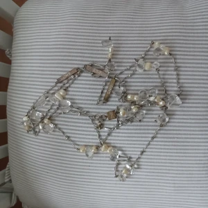Långt halsband med pärlor och kristaller - Elegant långt halsband med vita pärlor och klara kristaller. Kedjan är i silverfärg och har små detaljer som ger en lyxig känsla. Perfekt för att ge en extra touch till din outfit. SNÖ of Sweden