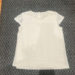 Vit spetsblus från Massimo Dutti - Elegant vit spetsblus från Massimo Dutti med korta ärmar och rund hals. Blusen har en fin spetsdesign och knappar i nacken för en stilren look. Perfekt för en somrig och fräsch stil. Två små fläckar men funkar ändå.