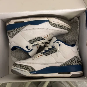 Nike Air Jordans i vitt och blått - Snygga Nike Air Jordans i vitt med blå detaljer och ett unikt mönster. Skorna har snörning och en klassisk design som passar perfekt för sneaker-älskare.