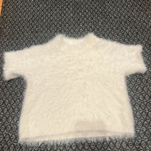 Vit fluffig tröja - Säljer en supermjuk och fluffig vit tröja med korta ärmar. Perfekt för att hålla sig varm och stilren under kyliga dagar. Tröjan har en enkel design som gör den lätt att matcha med olika outfits. Ett måste för garderoben! 🤍