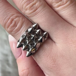 Silvrig ring med nitar - Cool och edgy silvrig ring med flera spetsiga nitar. Perfekt för att ge din stil en tuff touch. Ringen har en bred design som täcker en del av fingret och ger ett statement-utseende. Storlek 17,5 🤗Skick syns i bilder