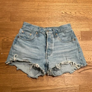 Blå jeansshorts från Levi's - Snygga blå jeansshorts från Levi's med fransiga kanter och klassisk. Modell 501. Mid waist och midjemåttet är 34 cm men de är en söm man kan sprätta upp där bak för att få en större midja. 