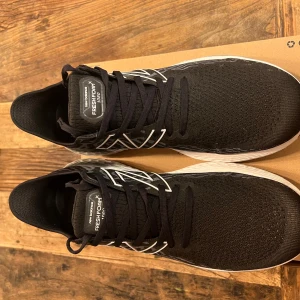 Svarta New Balance Fresh Foam löparskor - Snygga svarta New Balance Fresh Foam löparskor med vit sula och snörning. Skorna har en modern design med märkets logga på sidan och är perfekta för löpning och träning.