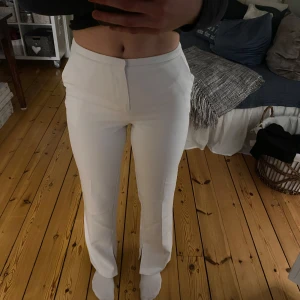 Vita kostymbyxor med slits - Snygga vita byxor med slits vid bensluten. De har en tight passform och är perfekta för en stilren look. Byxorna har en dragkedja framtill och är tillverkade i ett mjukt material som ger en bekväm känsla.