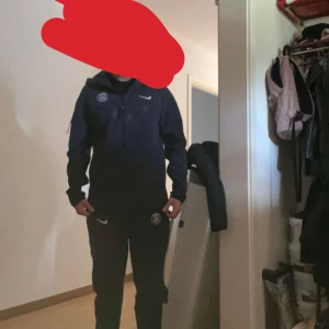 Mörkblå Nike Tech dress - Säljer en Grumt snygg mörkblå Nike Tech med PSG-logga på Huvtröjan.  Jackan har en dragkedja framtill och huva Perfekt. Byxorna dragkedja på båda sidorna för en avslappnad stil skick 8/10. 