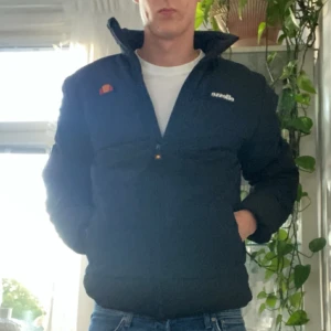 Svart pufferjacka från ellesse - Säljer en svart pufferjacka från ellesse. Den är perfekt för höst och vinter med sin varma och vadderade design. Jackan har en dragkedja framtill och långa ärmar. Den är i storlek herr M och passar bra för en normal passform. Perfekt för att hålla sig varm och stilig under de kallare månaderna!