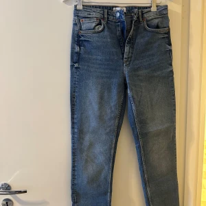 Blå jeans från Zara - Säljer ett par snygga blå jeans från Zara i storlek 38. De har en klassisk design med dragkedja och knapp framtill. De har en slits på neder delen av benen.