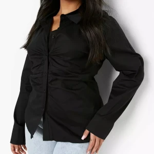 Ny svart skjorta med knappar - En helt ny stilren svart skjorta med långa ärmar och knappar framtill. Skjortan har en snygg rynkad detalj som ger den en unik look.