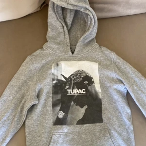 Tupac hoodie grå - Tupac hoodie grå, i använt skick. Storlek XS. Snören till luvan saknas och bilden är lite sliten. 