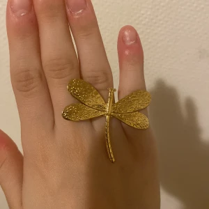 Guldig trollslända ring - Säljer en supercool guldfärgad ring formad som en trollslända. Den är stor och iögonfallande, perfekt för att ge lite extra bling till din outfit. Ringen är i nyskick och passar perfekt för både vardag och fest. 
