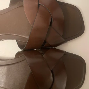 Bruna sandaler från H&M - Säljer ett par snygga bruna sandaler från H&M. De har en stilren design med korsade remmar och en fyrkantig tå. Perfekta för sommaren, använda men i bra skick! Dem ör i storlek 38 och har har nu 39 så lite små och knappt använda 😇🥰