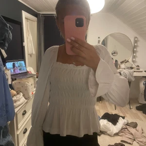 Vit blus med långa ärmar - Säljer en superfin vit blus med långa ärmar. Den har en smockad design som ger en snygg och bekväm passform. Blusen är en söt volangdetalj längst ner. Den är gjord i ett lätt och luftigt material. Den är i storlek XS och den HM