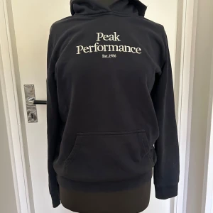 Svart hoodie från Peak Performance - Säljer en snygg och bekväm svart hoodie från Peak Performance. Den har en klassisk design med vit text på bröstet. Perfekt för både vardag och chill.