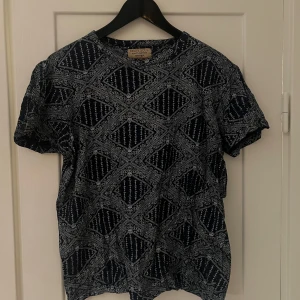 Mönstrad t-shirt från Brave Soul - Säljer en snygg t-shirt från Brave Soul i storlek M. Den har ett coolt mönster i mörkblått och vitt som ger en unik look. Perfekt för både vardag och fest! T-shirten är kortärmad och gjord i ett bekvämt material.
