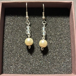 Eleganta örhängen med pärlor och glaspärlor - Säljer ett par eleganta örhängen med en stilren design. De har en vacker kombination av vita pärlor och klara glaspärlor som hänger i en silverfärgad kedja. Perfekta för både vardag och fest!⚜️