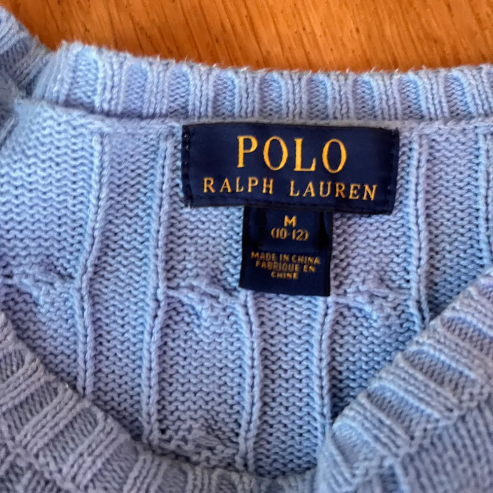 Säljer en snygg blå stickad tröja från Polo Ralph Lauren. Den har ett klassiskt flätmönster och är perfekt för både höst och vinter. Tröjan är långärmad och har ribbade muddar vid ärmslut och nederkant. Superfin och stilren!. Tröjor & Koftor.