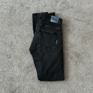 Svarta jeans från Scotch & Soda - Säljer ett par snygga svarta jeans från Scotch & Soda. De har en klassisk design med en knapp och dragkedja framtill. Jeansen är i storlek 16 och har en stilren look med en liten detalj i form av blå sömmar vid back ficka. 