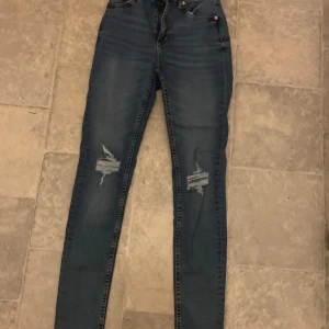 Blå jeans med slitningar från lager157 - Snygga blå jeans från lager 157 med slitningar på låren. De har en tight passform och är perfekta för en avslappnad stil. Klassisk femficksdesign och knappgylf. Materialet är stretchigt. Saknar lapp men är som S 
