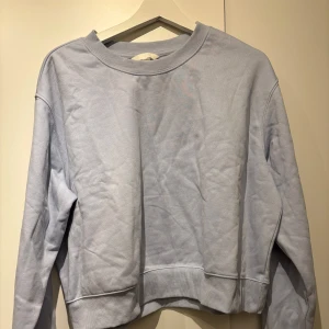 Ljusblå sweatshirt - Säljer en ljusblå sweatshirt med rund hals och långa ärmar. Tröjan har ribbade muddar vid ärmslut och nederkant, vilket ger en bekväm passform. Perfekt för en avslappnad stil.