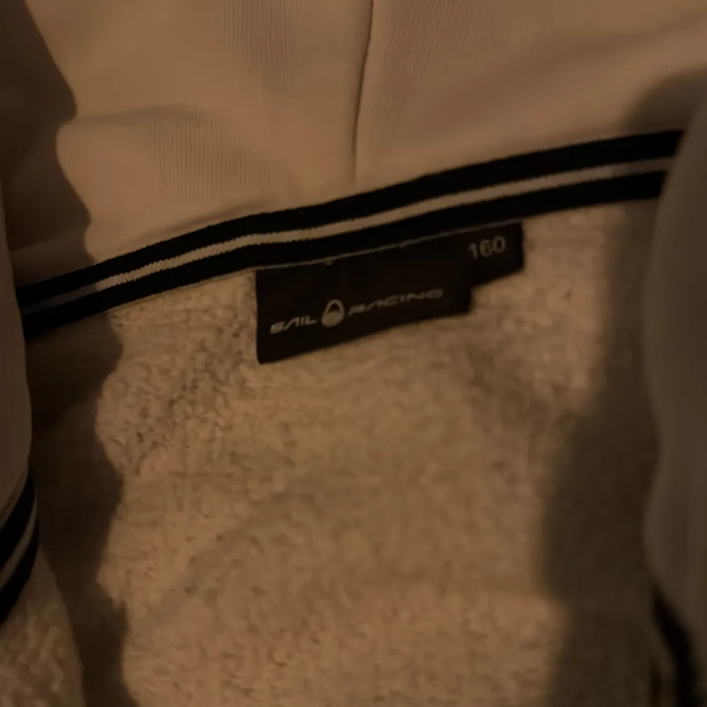 Säljer en beige fleecejacka från Sail Racing med huva och dragkedja framtill. Jackan har en enkel design med en liten logotyp på bröstet. Perfekt för kyliga dagar.. Takit.