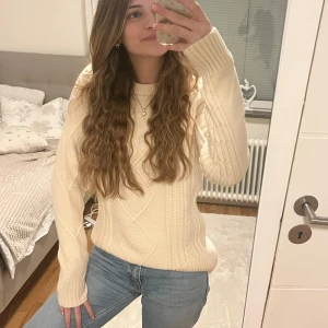 Beige stickad tröja - Mysig beige stickad tröja med ett klassiskt flätmönster. Tröjan har långa ärmar och en rund halsringning, perfekt för kyligare dagar. Passar bra till jeans eller kjol för en avslappnad look. Nästan helt ny, använd en gång.