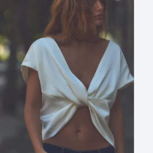 Vit omlott topp - HELT NY LAPPEN ÄR KVAR Snygg vit omlott topp med korta ärmar och knytning framtill. Perfekt för en stilren och modern look. Toppen är croppad och har en djup v-ringning. Man kan ha den bak och fram silkes