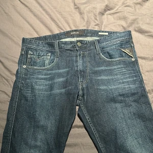 Blå jeans från Replay - Snygga blå jeans från Replay med klassisk femficksdesign och knappgylf. Jeansen har en lätt tvättad look och är perfekta för en avslappnad stil. Märkesdetaljer syns på bakfickan och linningen.