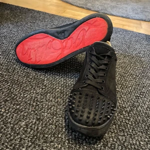 Christian Loubitins  - Snygga svarta sneakers med nitar på ovansidan och röd sula. Skorna har snörning och en stilren design som passar perfekt för en trendig look.