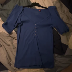 Blå topp från Esprit - Säljer en blå topp från Esprit med knappar framtill. Toppen har en v-ringad design. Perfekt för en stilren look.